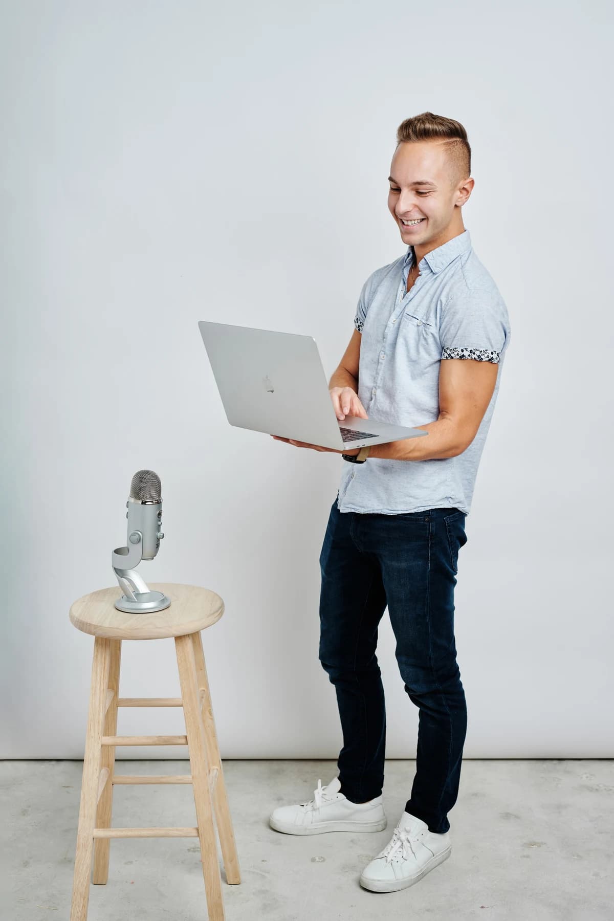Jordan holding a laptop beside a microphone on a wooden stool.