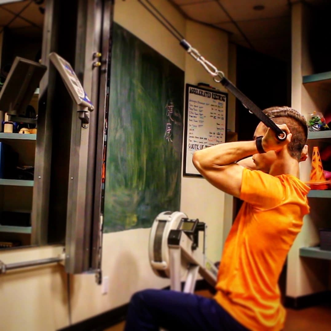 Jordan in an orange shirt training with a cable machine in a gym.