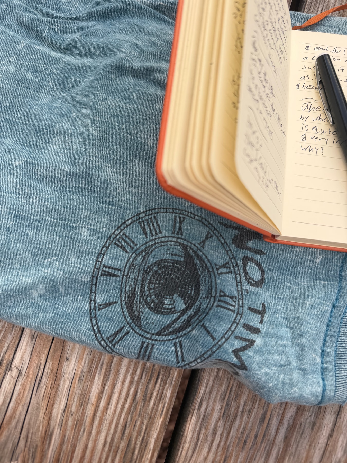 An open orange notebook and pen resting on blue fabric printed with a clock.