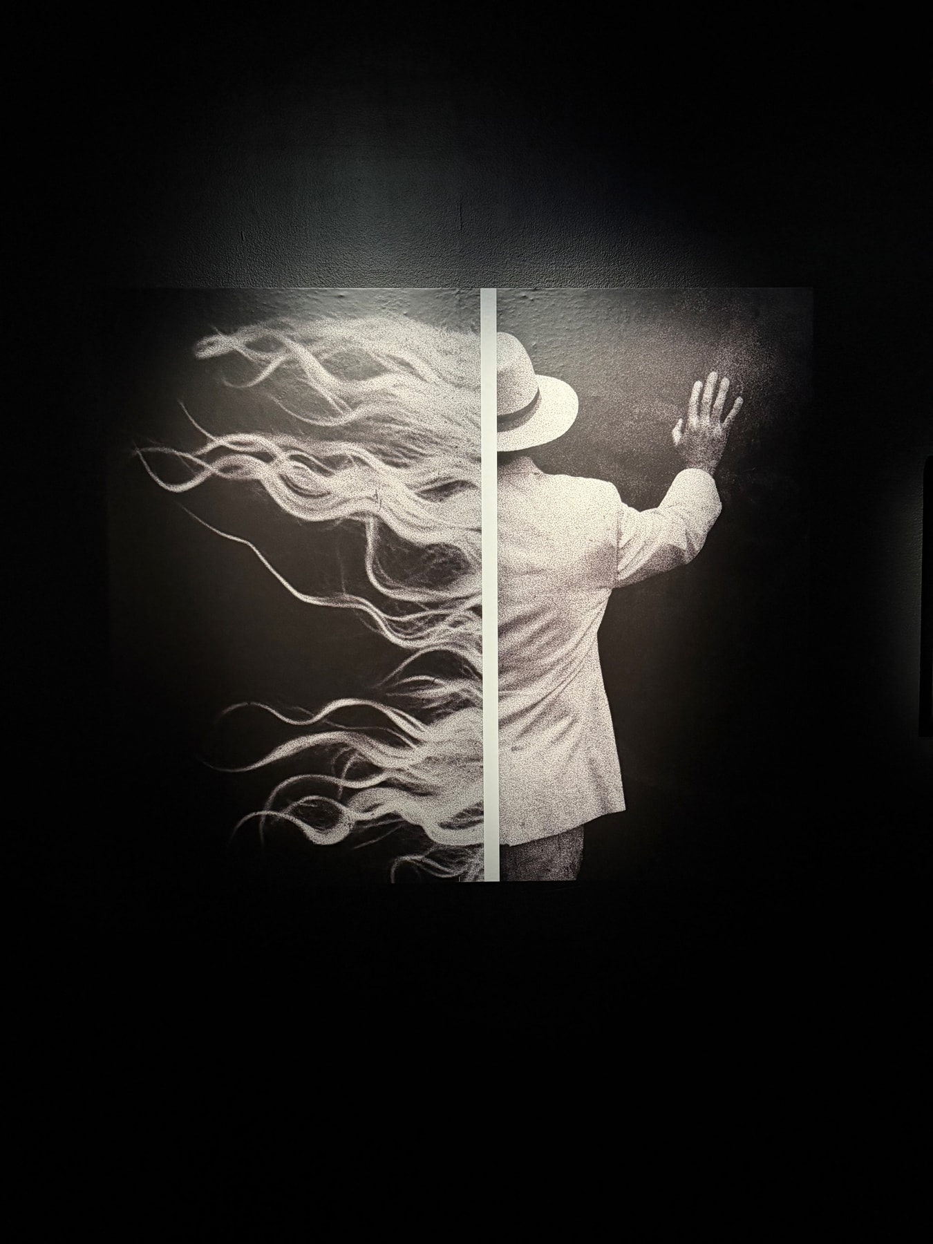 A photograph of Joakim Möller's work: a figure in a hat, a raised hand, and flowing strands divided by a vertical white line.