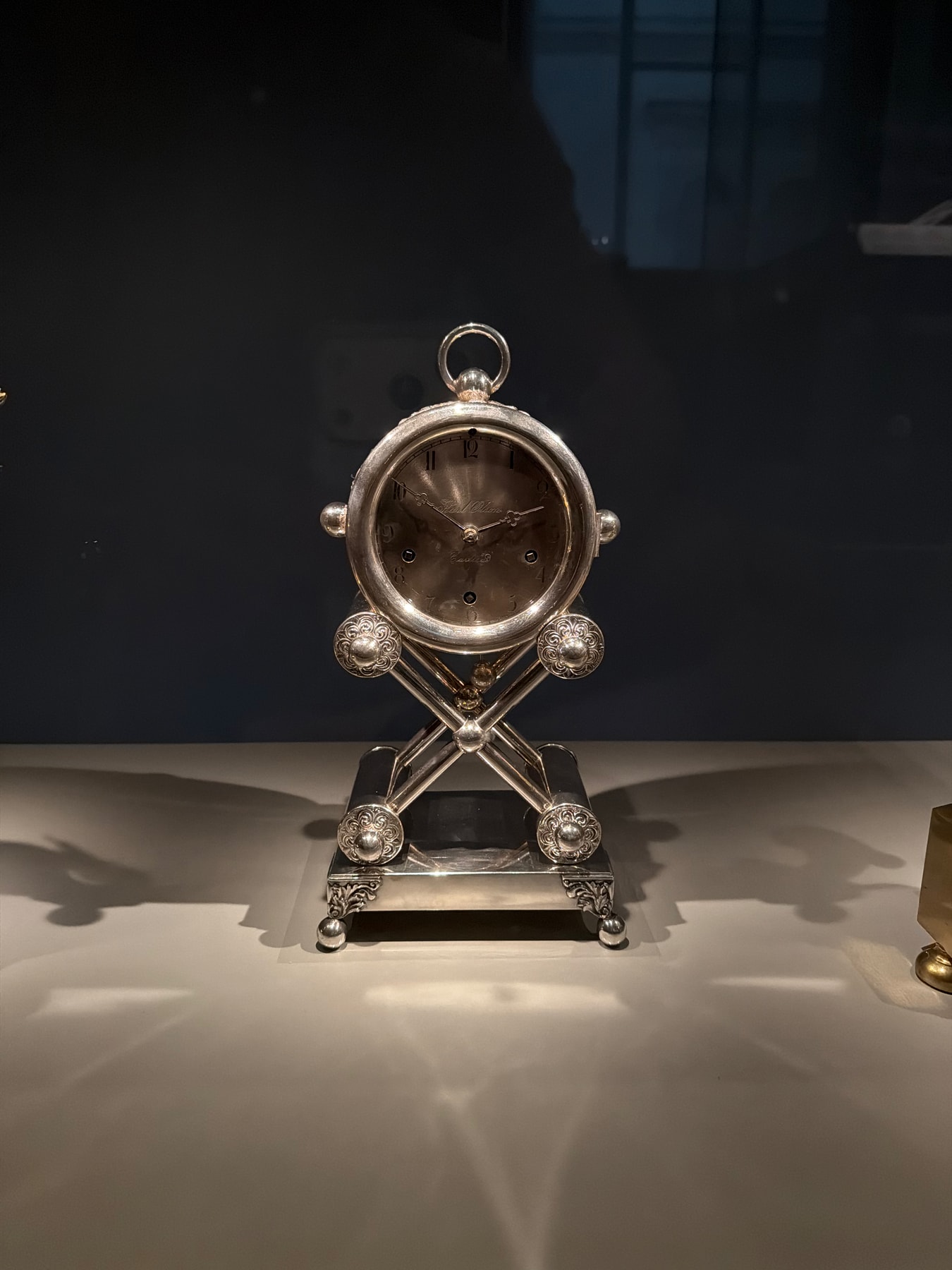 An ornate silver clock illuminated against the dark wall of a museum display.