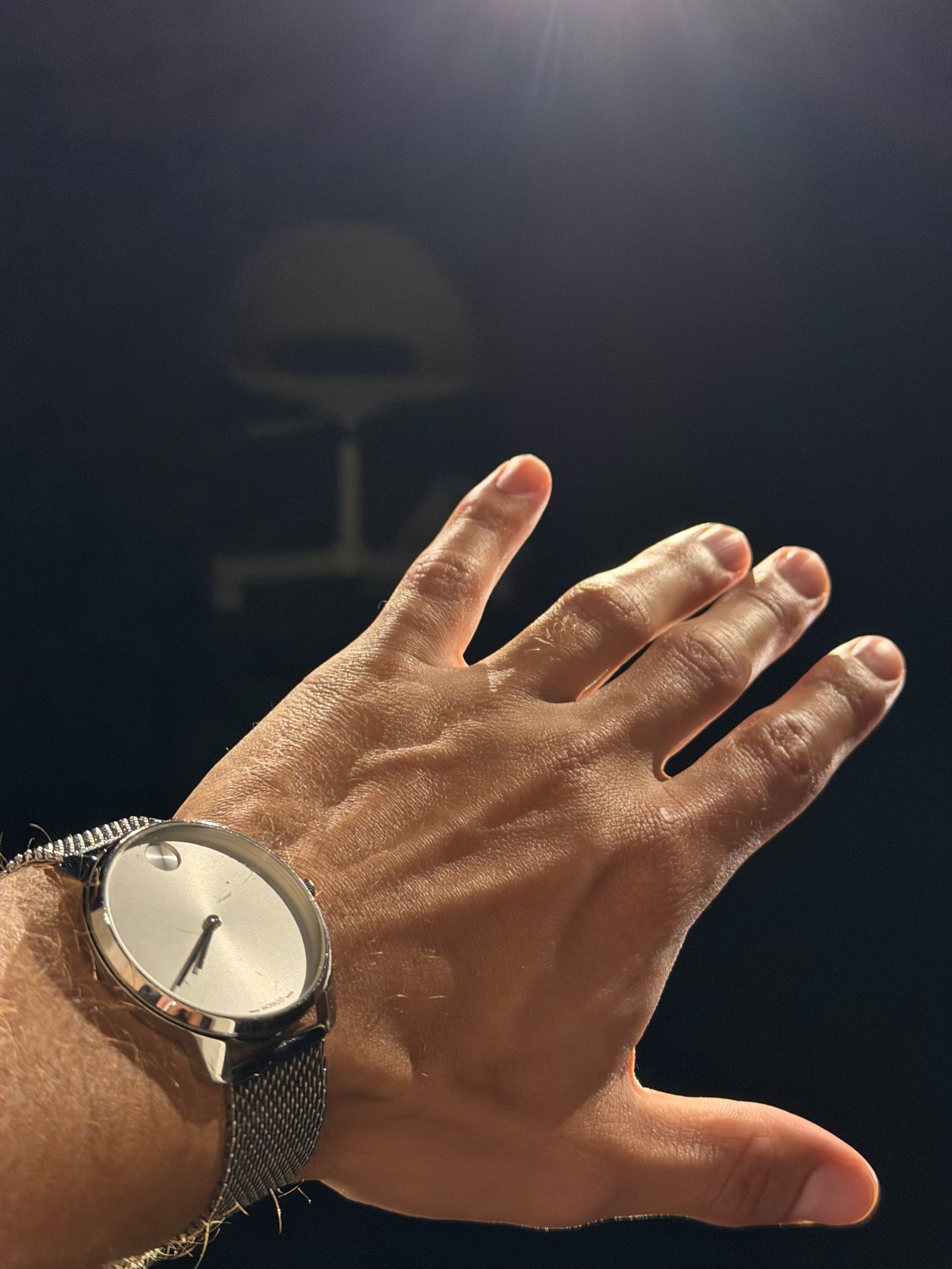 A hand wearing a silver watch reaches into a beam of light.