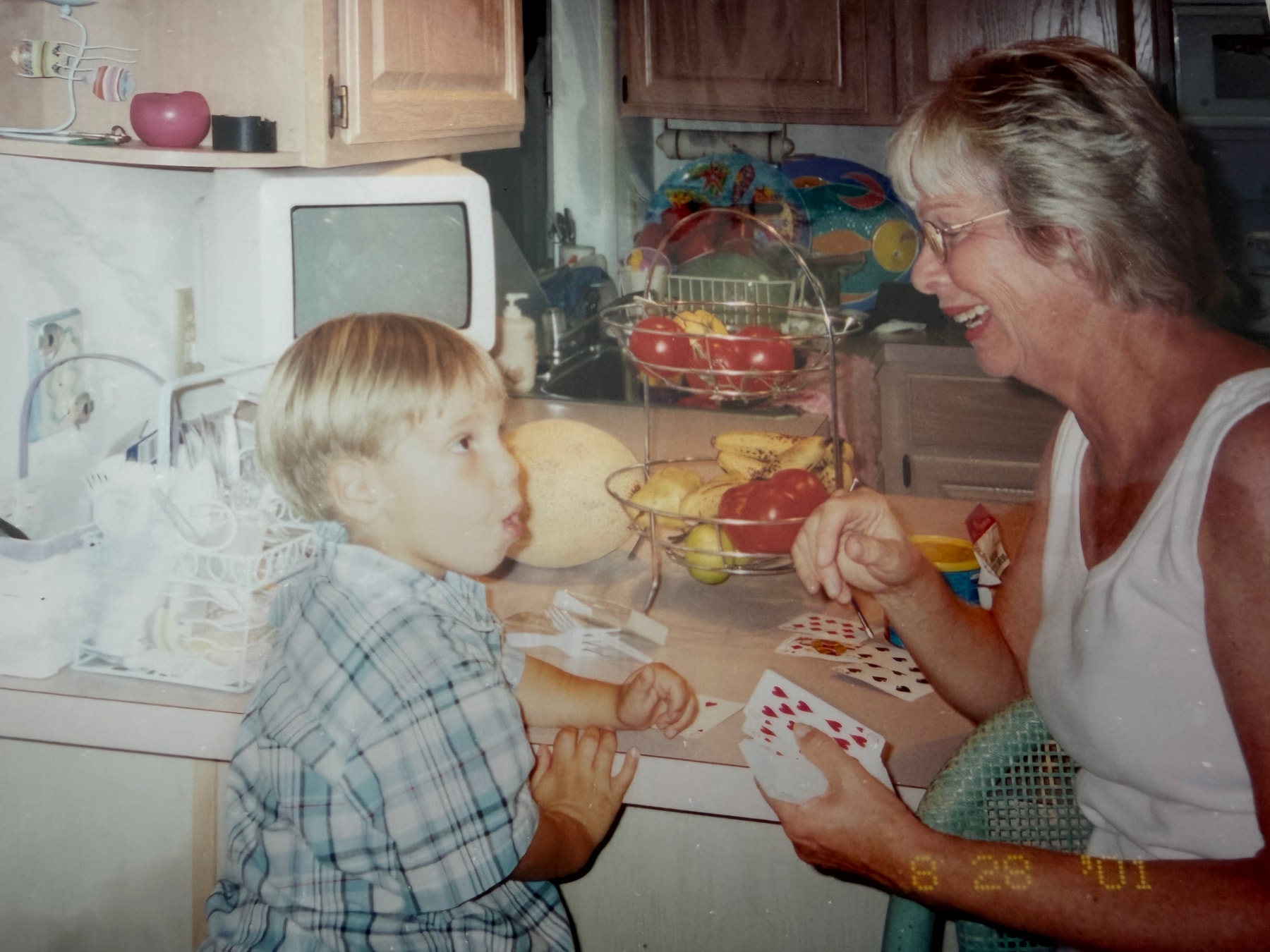A childhood photograph of a young child and an older woman sharing a moment over playing cards in a kitchen.